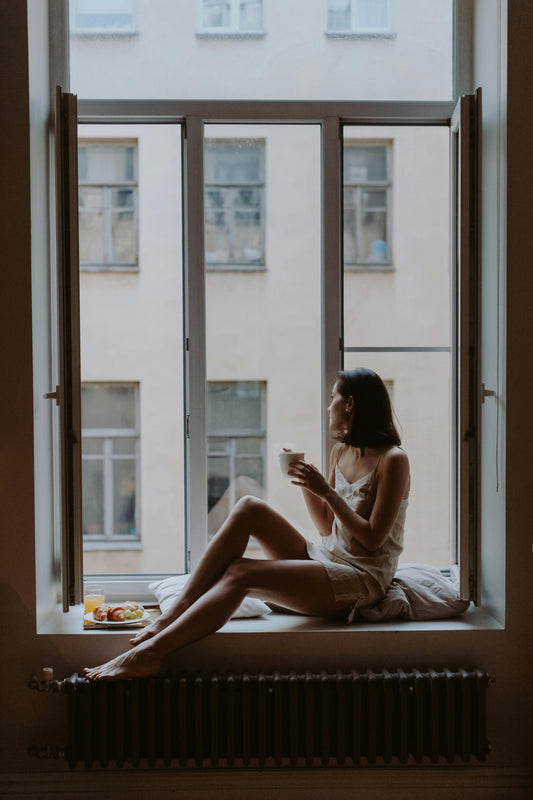 Mujer descansando en un rincón íntimo con luz natural suave.
