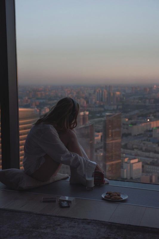 Mujer sentada junto a la ventana con luz suave de tarde, respirando con calma