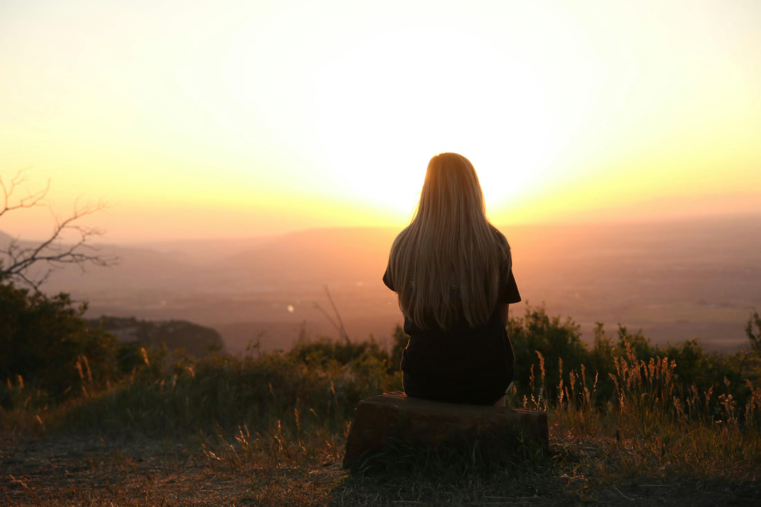 Mujer sentada en silencio contemplando el atardecer desde una colina, en soledad consciente y conexión consigo misma