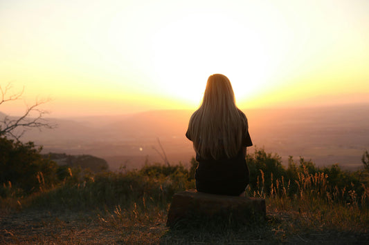 Mujer sentada en silencio contemplando el atardecer desde una colina, en soledad consciente y conexión consigo misma